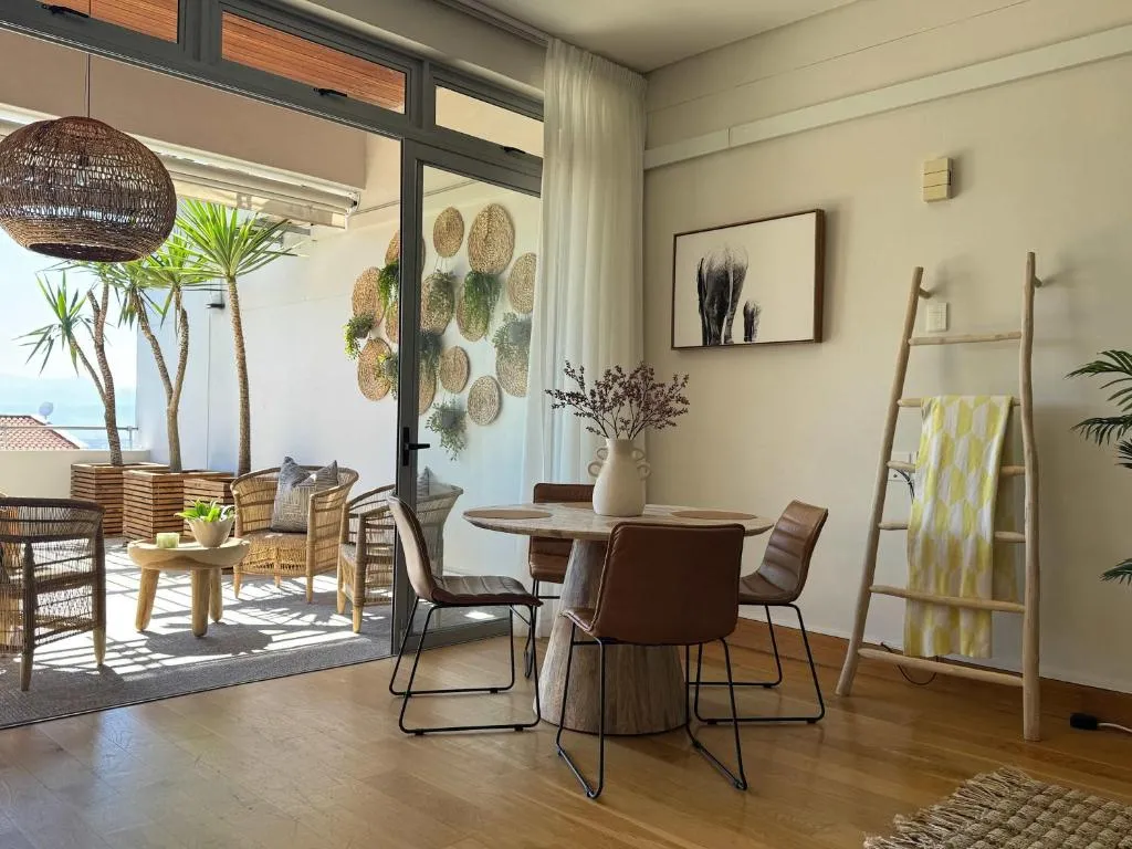 Open-plan dining area with a round wood table flowing onto a plant-filled terrace