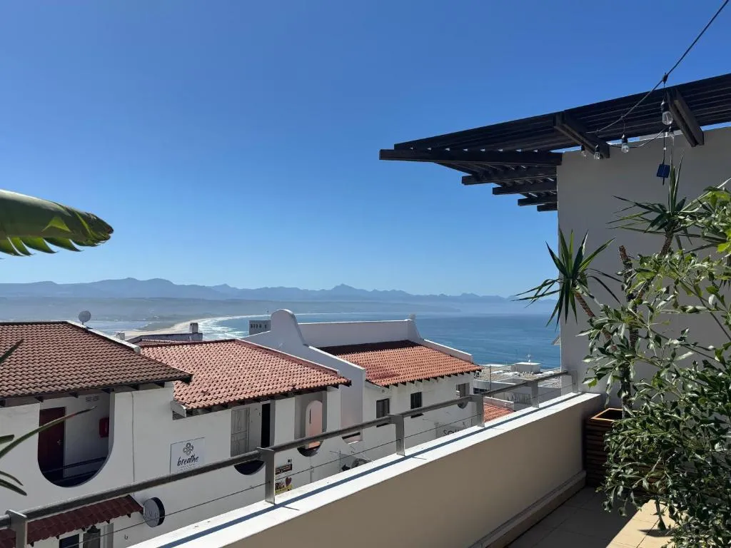 Terrace corner with palms framing tiled rooftops, a stretch of beach and distant mountains