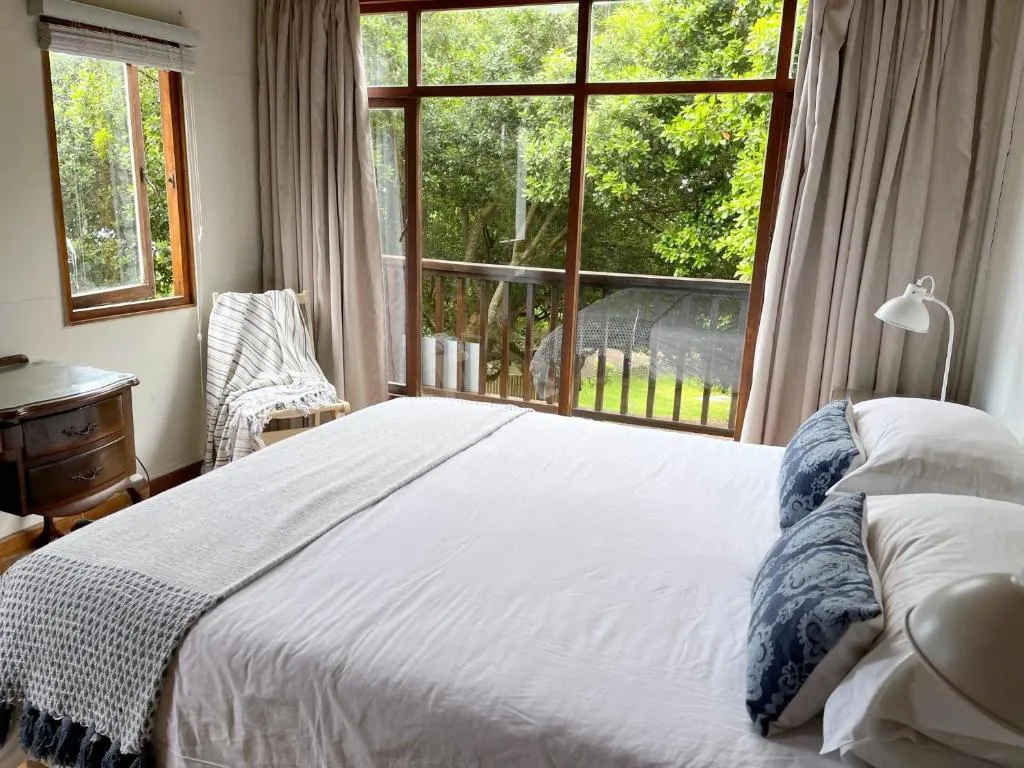 Bedroom with glass doors onto a balcony overlooking dense forest canopy