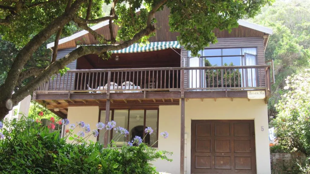 Wood-clad chalet with a shaded balcony over flowering agapanthus and garden shrubs