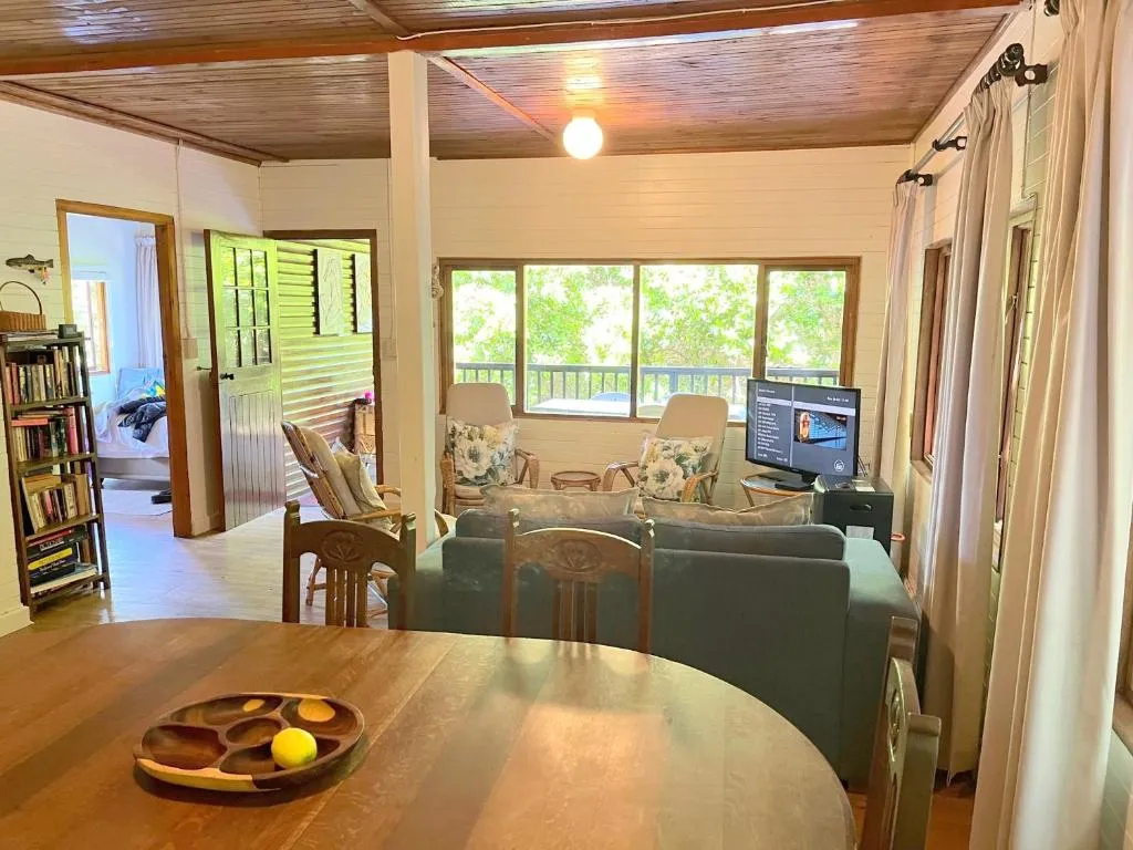 Open living and dining area with bookshelf, cane chairs and a treetop-view balcony