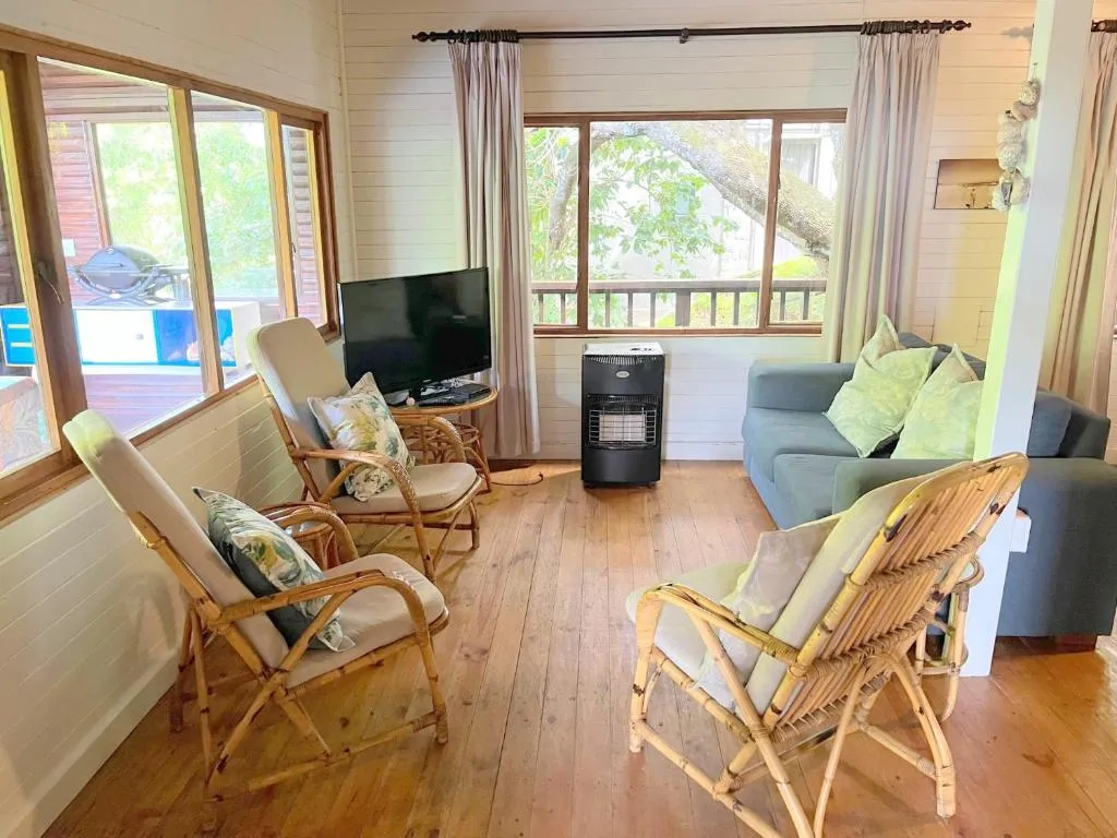 Living room with rattan armchairs, a gas heater and a braai visible on the deck outside