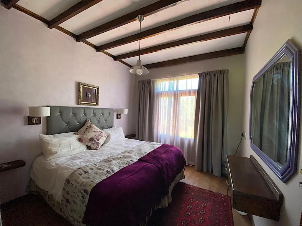 Guest bedroom with a grey tufted headboard, purple throw and beamed ceiling