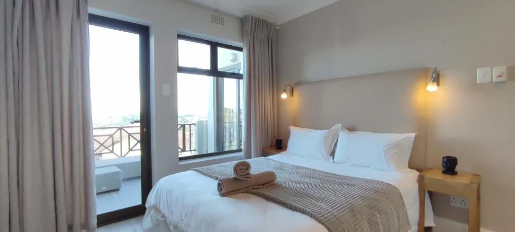 Bedroom with white bed linen, a sliding door and window facing the hillside