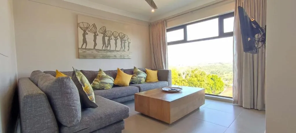 Living room with a grey sectional sofa and a large window looking over green hillside