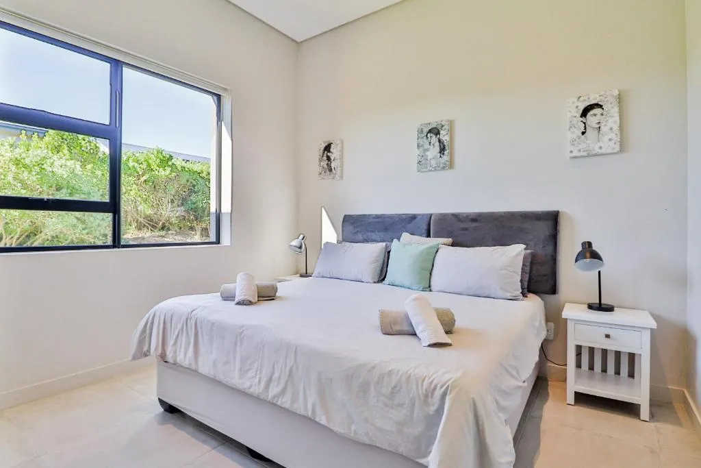 Bedroom with king bed and a wide window looking onto indigenous bush and fynbos