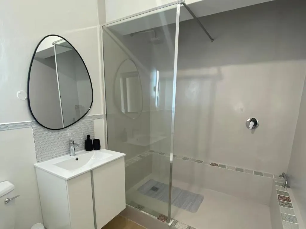 En-suite bathroom with a glass-walled shower, oval mirror and white vanity