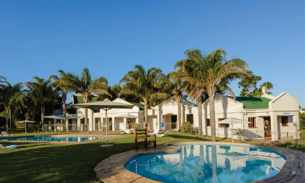 Cape-style estate buildings with green roofs, palm trees and a curved pool in the foreground