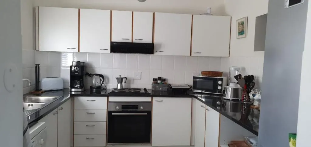 Galley kitchen with black countertops, built-in oven and stovetop, and overhead white cabinetry
