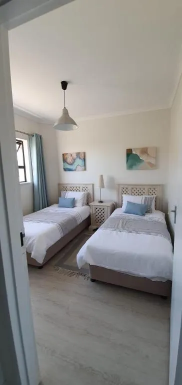 Twin bedroom with matching upholstered headboards, coastal artwork and a pendant light
