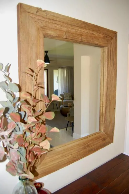 Wooden-framed mirror reflecting an open-plan lounge with red armchairs and tiled floors