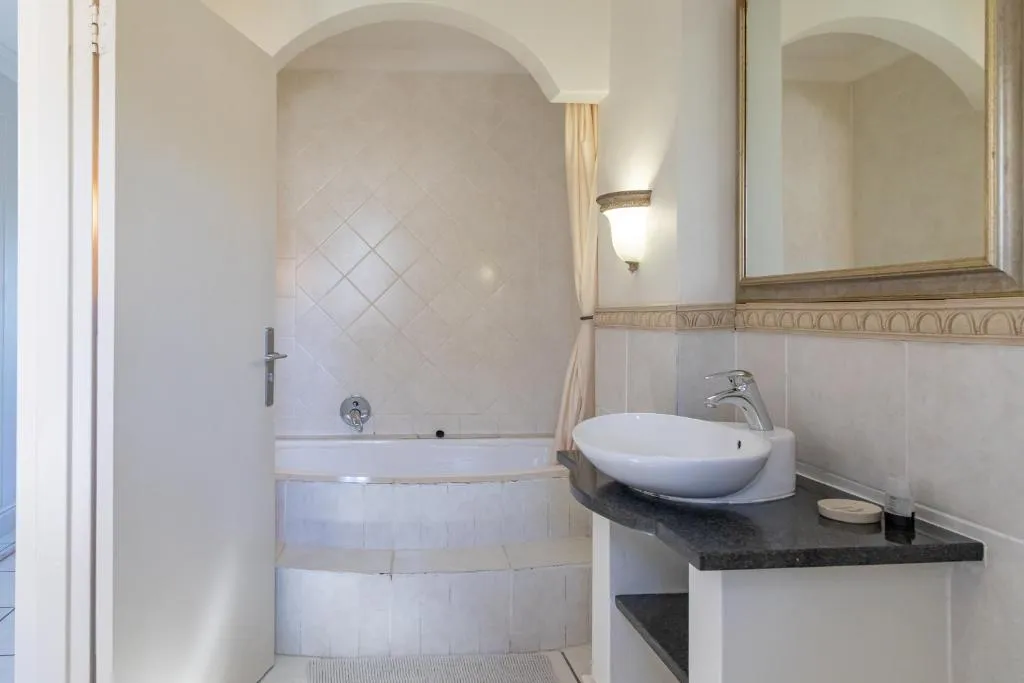 Bathroom with a corner bathtub in an arched alcove and a vessel sink on a dark countertop
