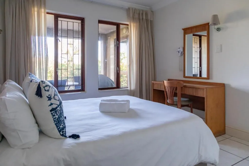 Bedroom with white bedding, navy accent pillow, and wood-framed windows onto a balcony