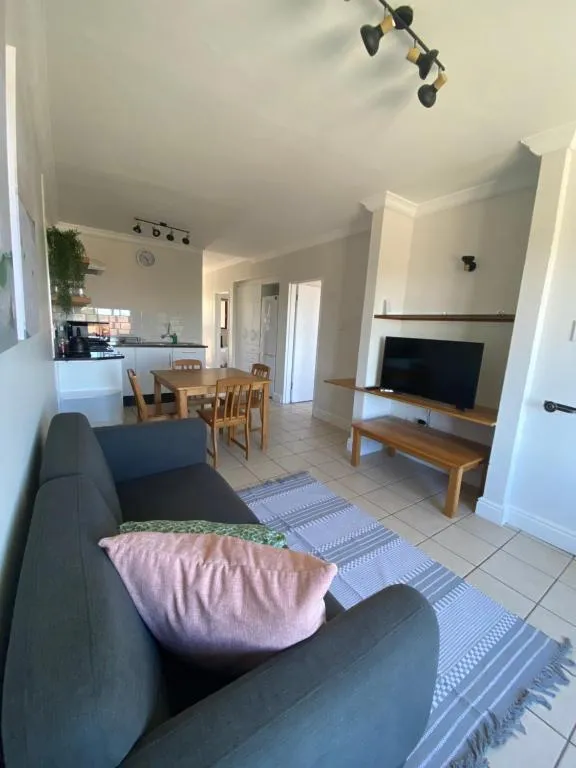 Open-plan lounge with a grey sofa, wall-mounted TV, and a dining table by the kitchen
