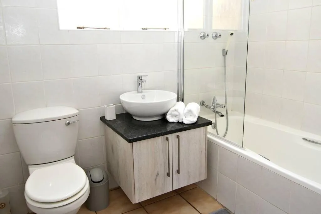 Bathroom with a vessel sink on a dark countertop, bathtub with shower and toilet