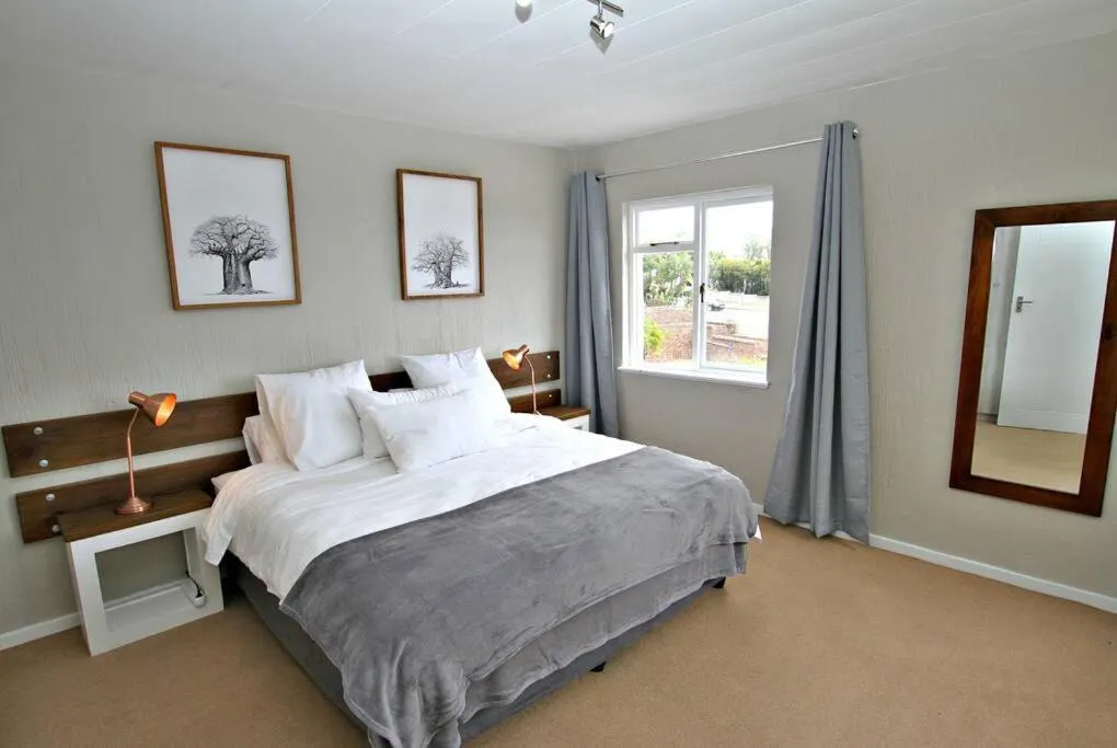 Bedroom with a grey-upholstered double bed, bedside lamps and a street-facing window