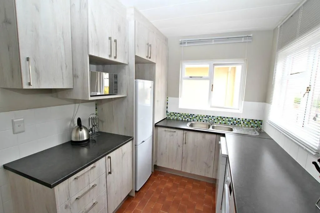 Galley kitchen with light wood cabinets, a white fridge-freezer and a green mosaic splashback