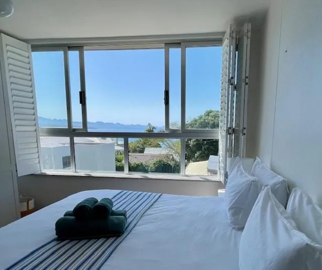 Bedroom with white plantation shutters open to a sea and mountain view over the street