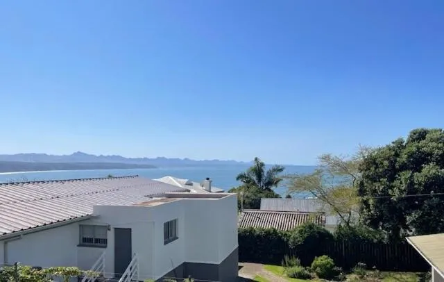White house exterior with a pitched roof set above the bay, mountains beyond