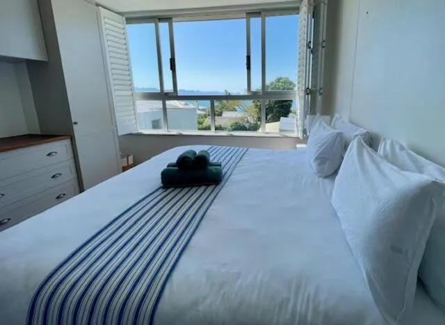 Second bedroom with striped bed linen and a shuttered window overlooking the bay