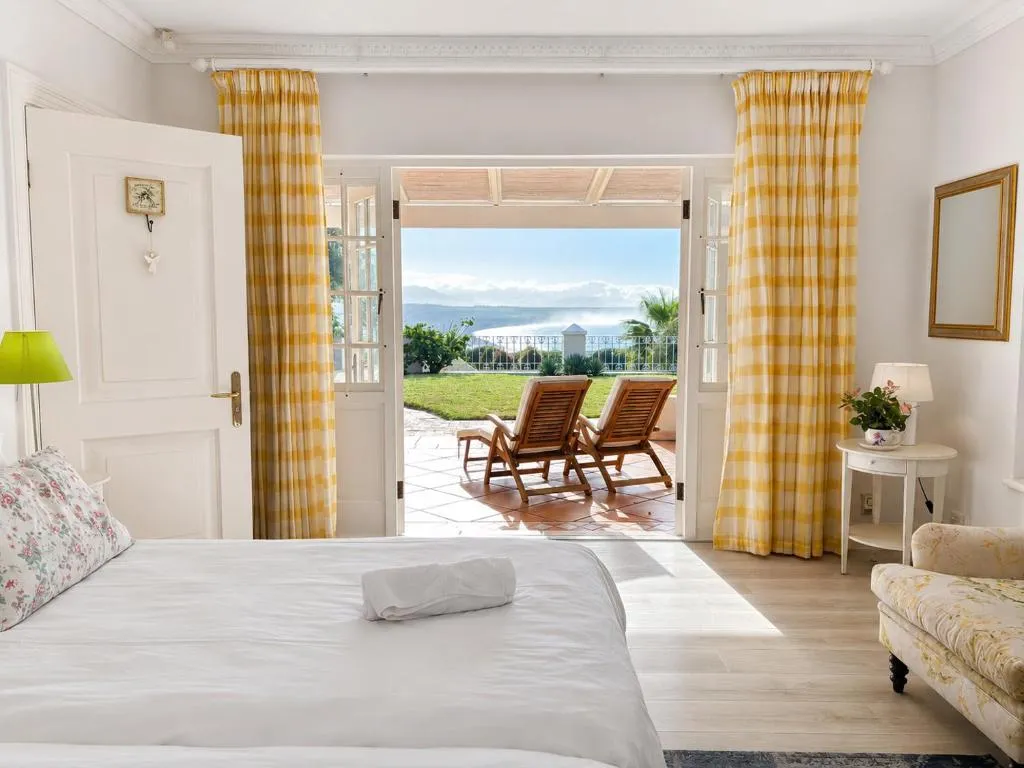 Bedroom with gingham curtains framing French doors onto a sea-view patio