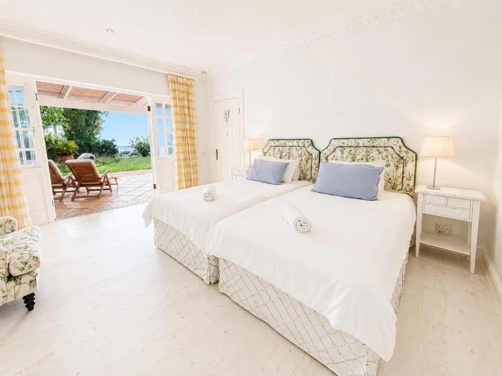 Twin bedroom with floral headboards and French doors opening onto a sea-view patio