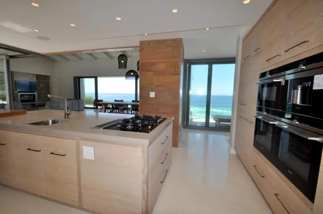 Open-plan living room with black leather sofas and floor-to-ceiling windows framing sea views on both sides