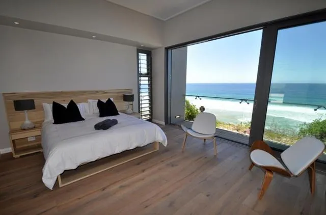 Main bedroom with a full glass wall opening onto a balcony overlooking the ocean