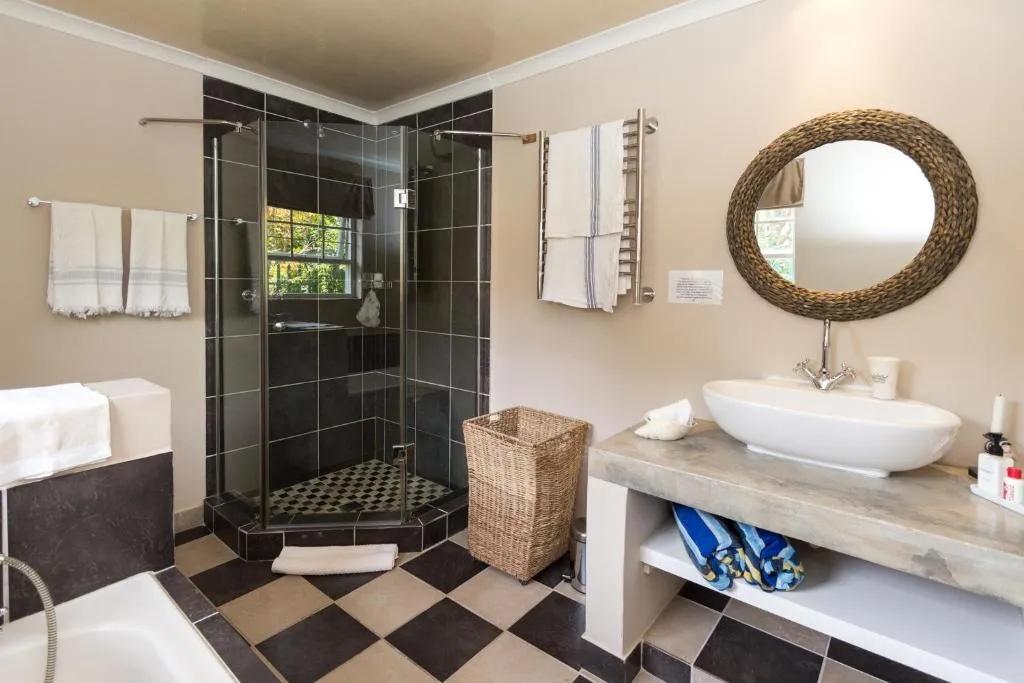 Bathroom with a chequered tile floor, glass shower, and a woven round mirror over the basin