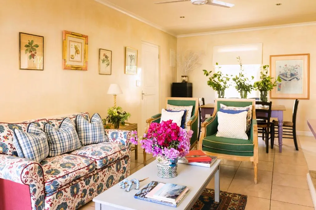 Living room with a floral sofa, green armchairs, and a dining table beyond