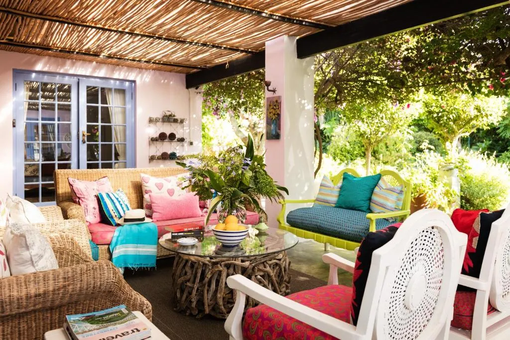 Reed-roofed veranda with wicker sofas, patterned cushions, and doors onto a lush garden