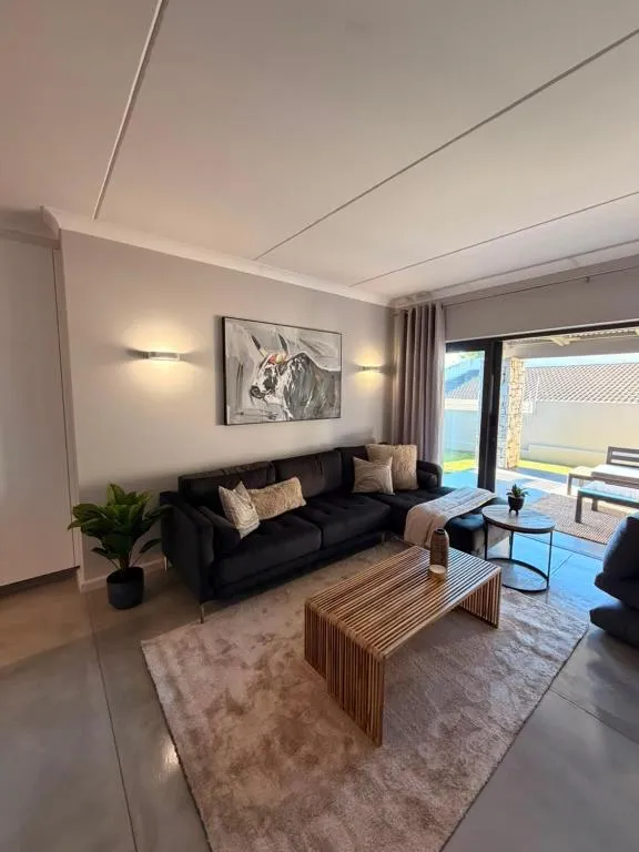Open-plan living room with black corner sofa, cow artwork and sliding doors to a paved patio