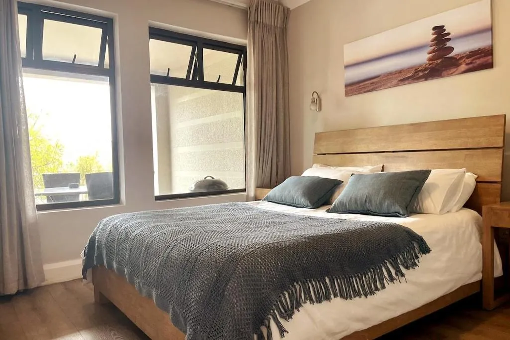 Bedroom with a wood-framed bed, grey knit throw, and a corner window looking onto the garden terrace