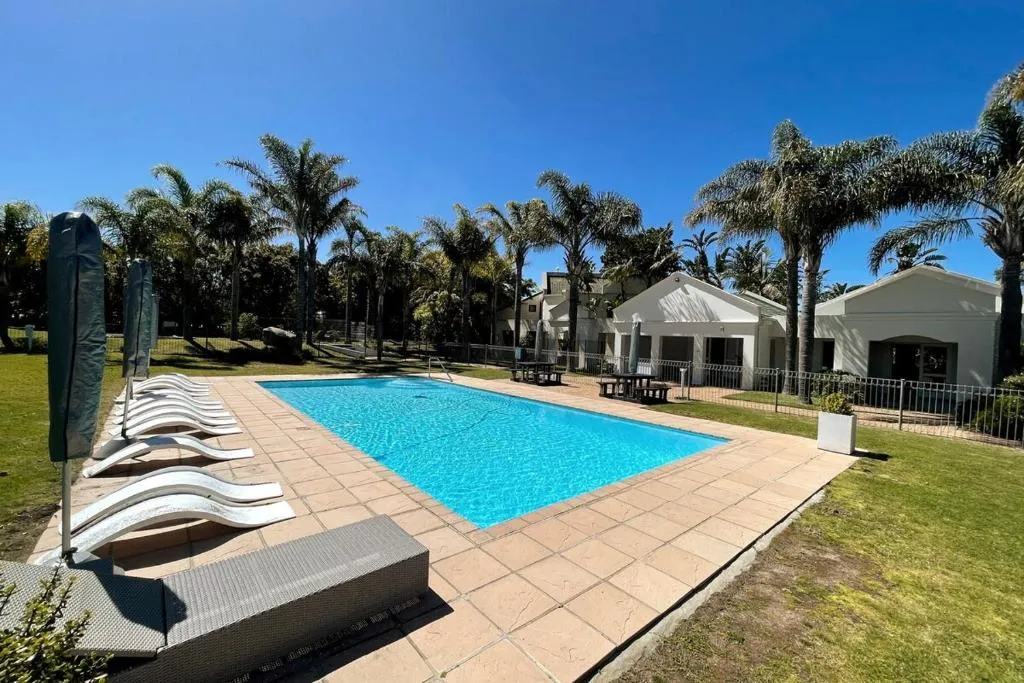 Communal pool with sun loungers and umbrellas set among palms beside the estate clubhouse