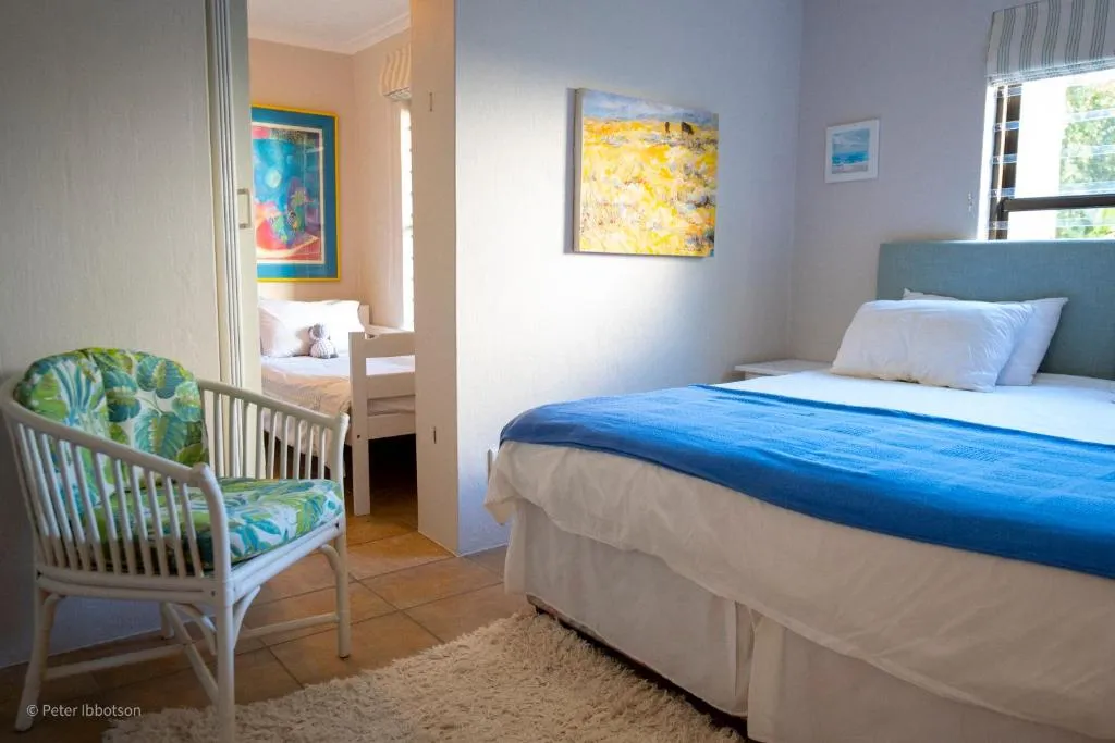 Bedroom with a blue upholstered headboard, rattan armchair and a doorway through to a twin room