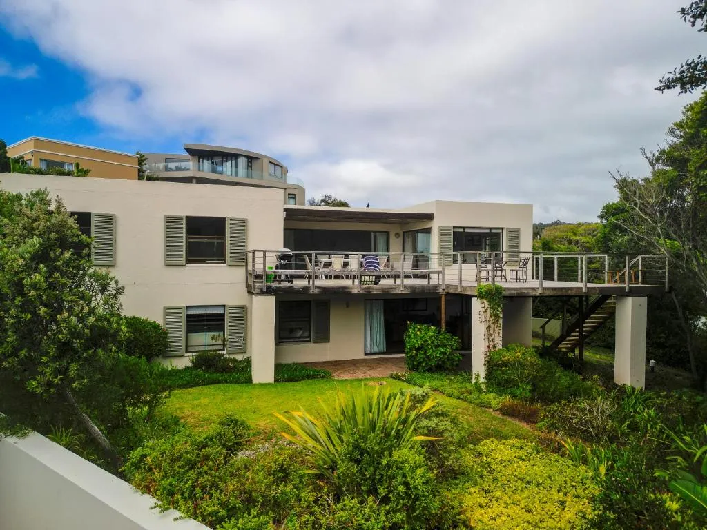 Rear elevation showing an upstairs balcony with a dining table and chairs above a garden lawn