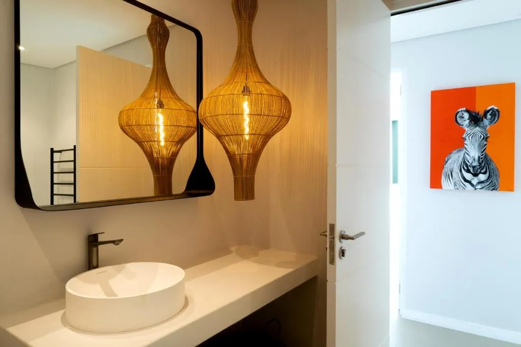 Bathroom with a round vessel basin, woven rattan pendant lights and a black-framed mirror