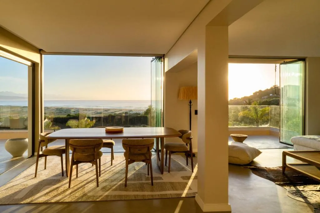 Dining table beside floor-to-ceiling glass doors framing an uninterrupted ocean view