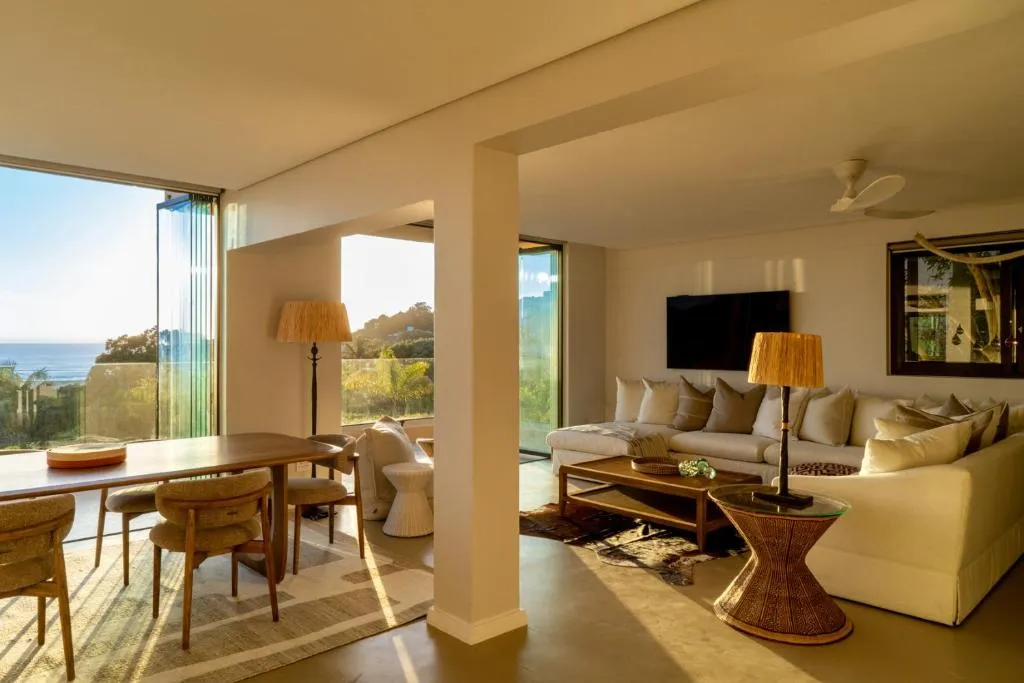 Open-plan living room with a white sectional sofa and a glimpse of the sea through the window