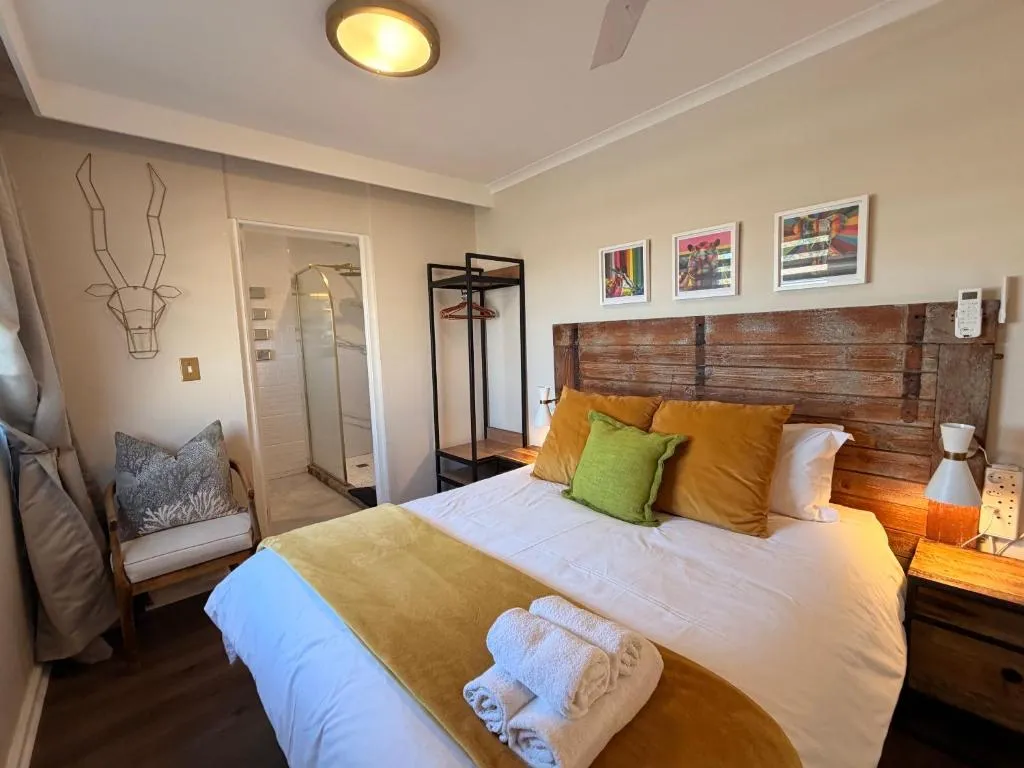 Bedroom with reclaimed wood headboard, gold cushions and a doorway to an en-suite shower