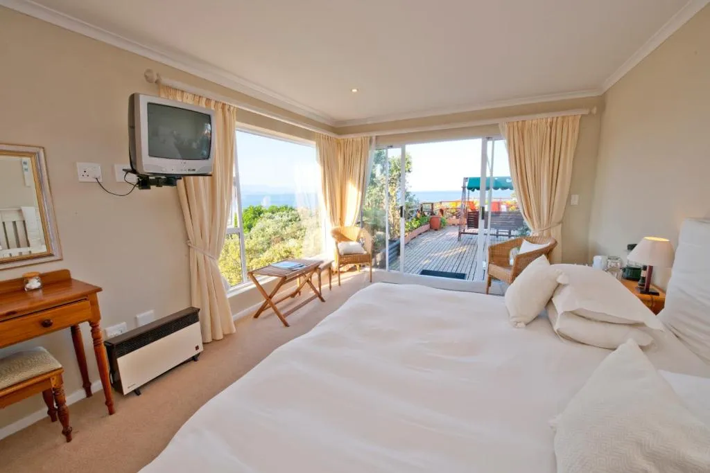 Bedroom with sliding doors onto a wooden deck with sea glimpses through trees