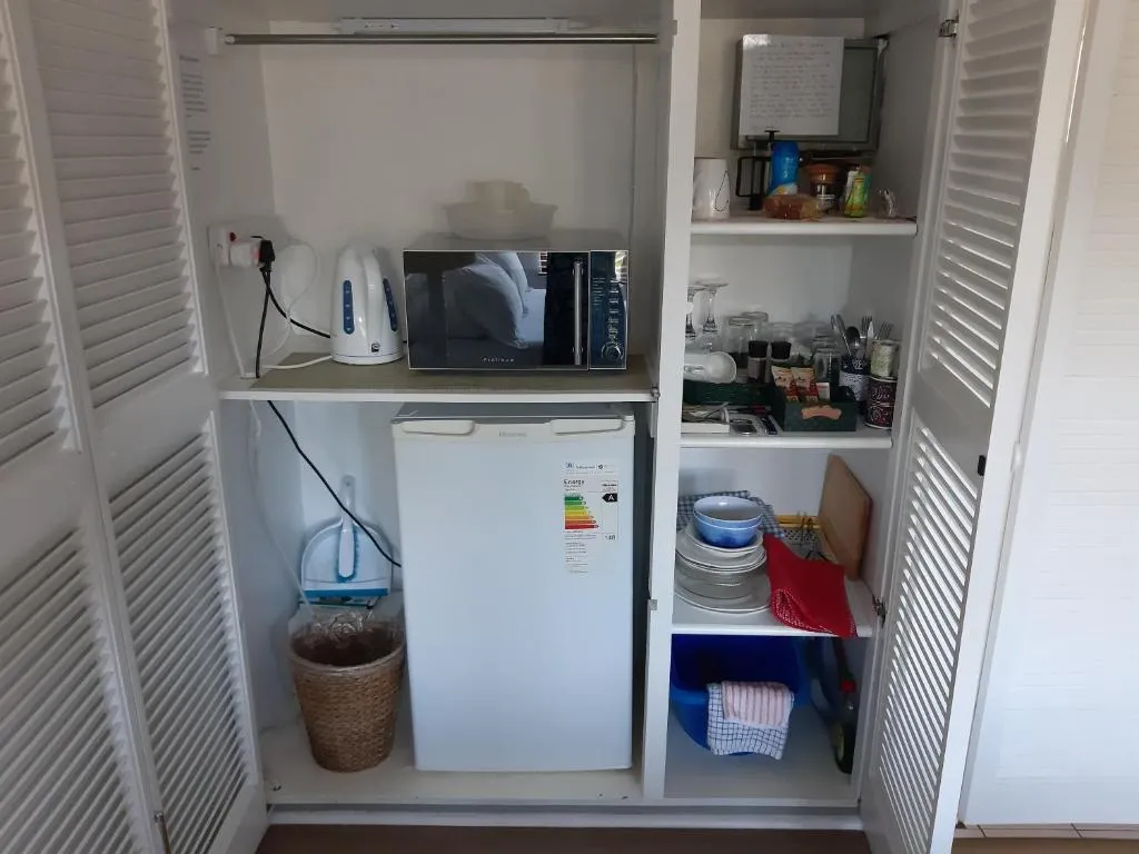 In-room kitchenette cupboard with a bar fridge, kettle, microwave and crockery