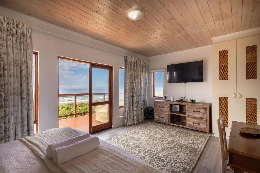 Bedroom with a private balcony door framing the ocean beyond dune vegetation
