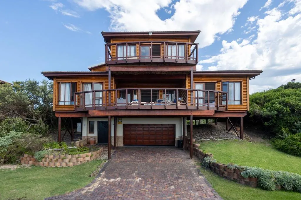 Three-storey timber-clad villa on stilts with wraparound balconies above a paved driveway