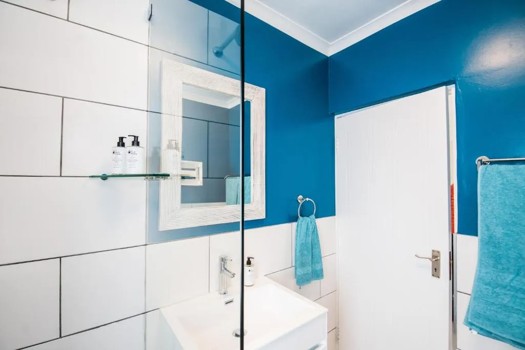 Bright blue bathroom with a wall-mounted vanity, mirror and glass shower screen
