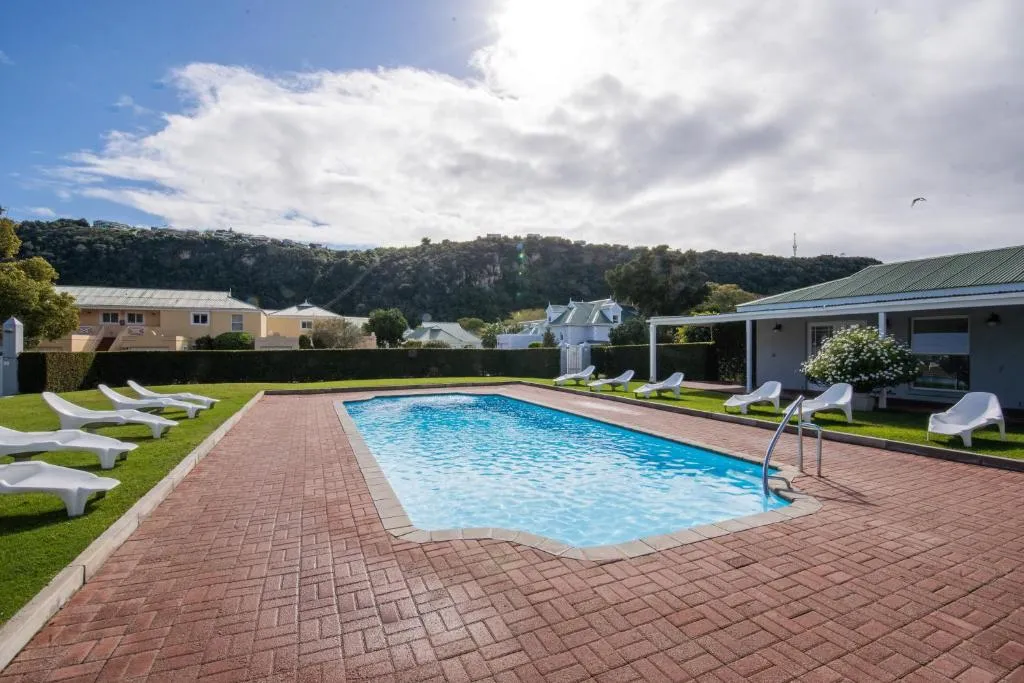 Shared estate swimming pool with loungers, lawn and hillside houses beyond
