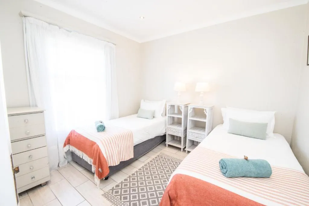 Twin bedroom with matching single beds, coral striped throws and bedside lamps