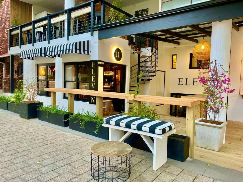 Street-facing entrance of Eleven hotel with a striped awning, bougainvillea and outdoor bench seating