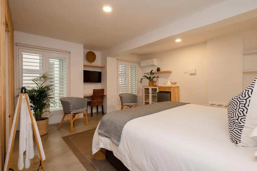 Guest room with a wall-mounted air conditioner, TV, work desk and shuttered windows