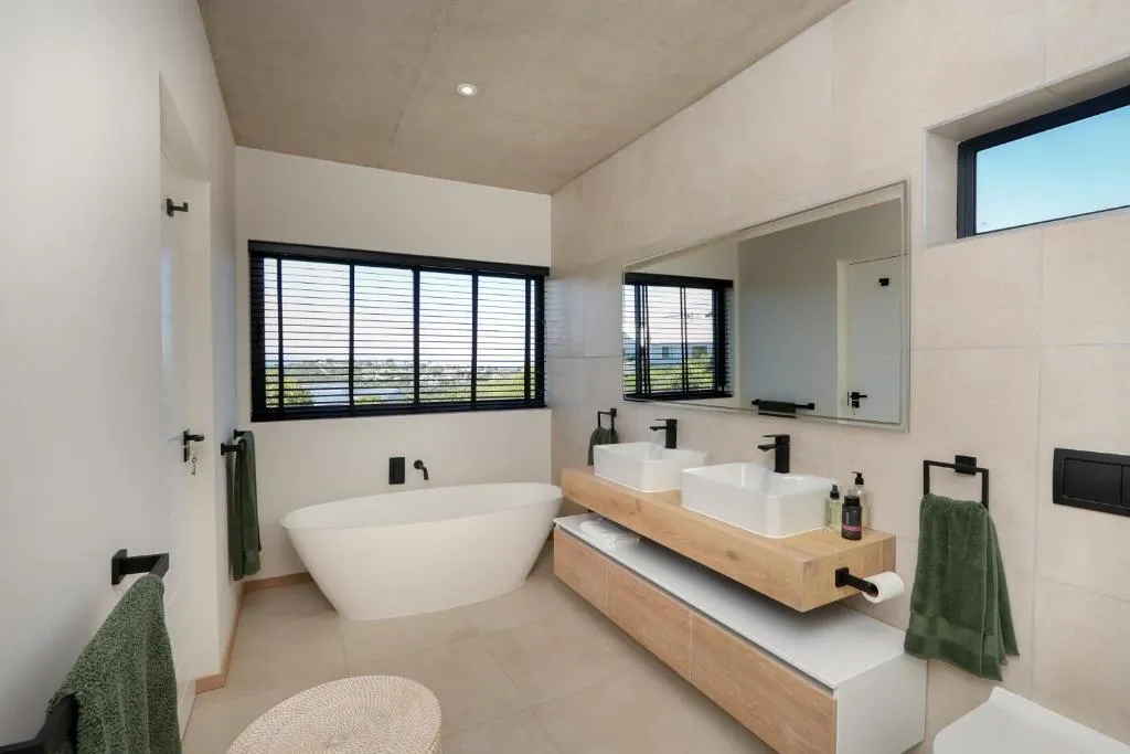 En-suite bathroom with a freestanding oval tub and double vessel-sink vanity beneath louvred windows